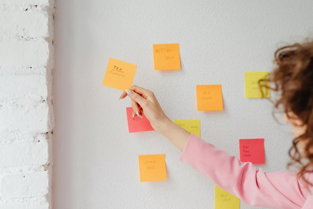 Woman organizing tasks using sticky notes on a wall, promoting productivity and planning.